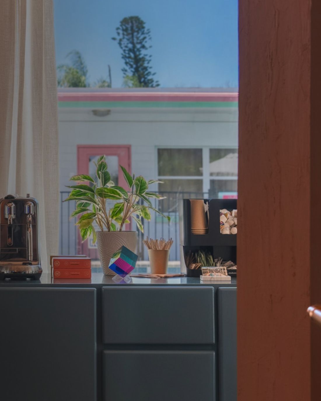 A doorway opening onto a unit with a coffee station and a view of a pink-trimmed building