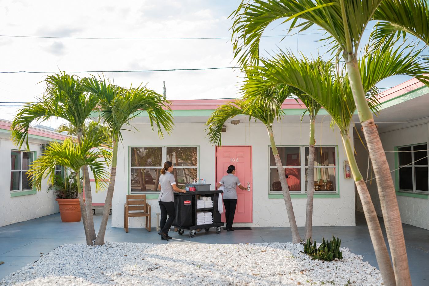 Two housekeepers with a linen cart at a pink motel door